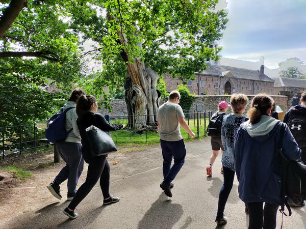 a group of students walking outside in the dunham massey park on a sunny day. They are heading towards an old brick buidling.