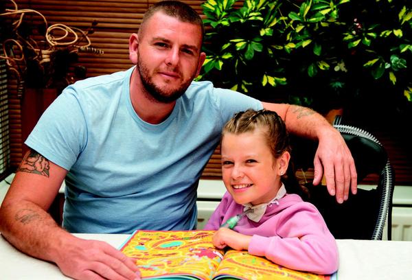 a man smiling sat next to a girl who is colouring on a piece of paper