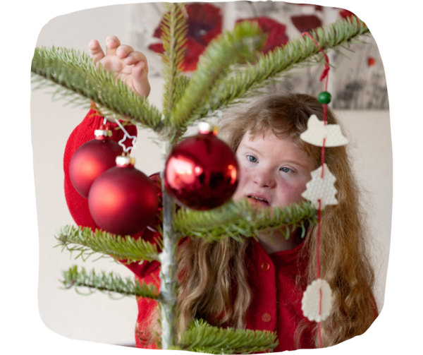 Christmas tree with red baubles in front of a girl with down syndrome looking up at the decorations. 