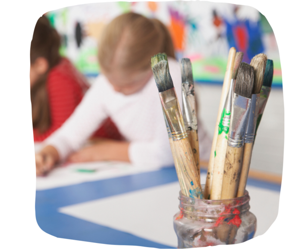 Dirty paintbrushes in a glass pot in front of a group of students painting