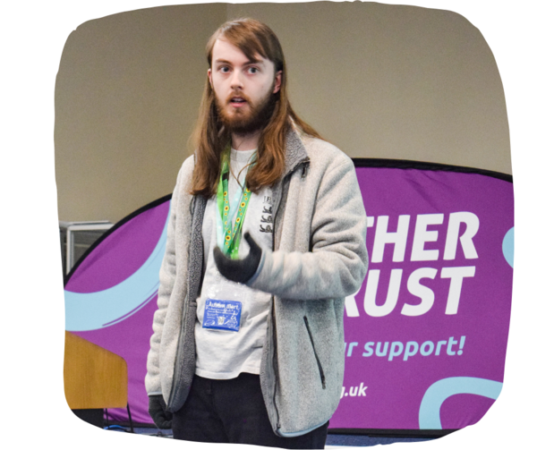 Man with long hair wearing a sunflower lanyard speaking in front of a room