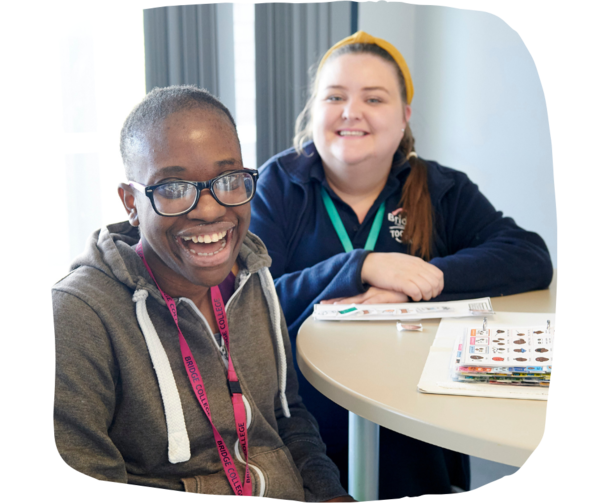 Student at teacher sitting down at a table in the cafeteria, both smiling. 