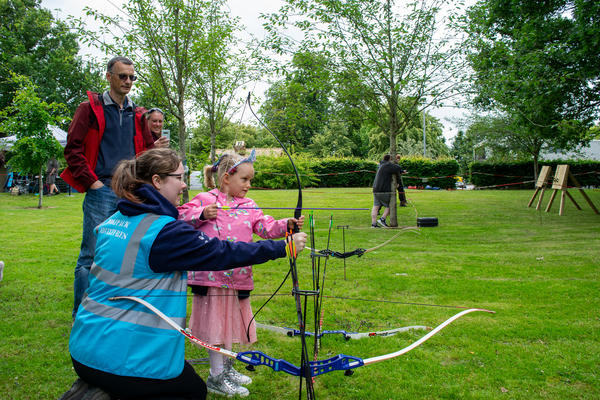 a young girl being shown how to fire an arrow from an archery bow
