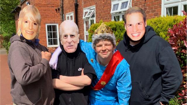 Students and staff posing for a photo, wearing Royal Family face masks, along with a student dressed as Queen Elizabeth II