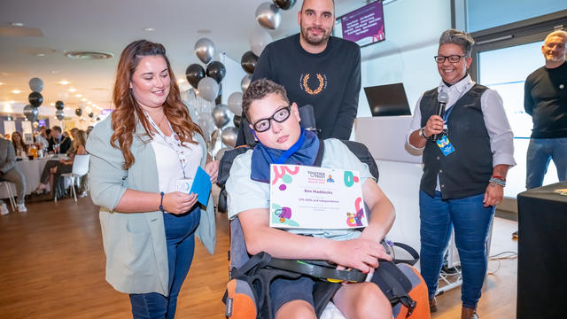 A young man in a wheelchair posing for a photo with his certificate between three staff members from the Together Trust