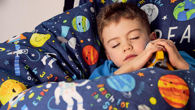 Young boy sleeping on a bed with space themed bedding. 