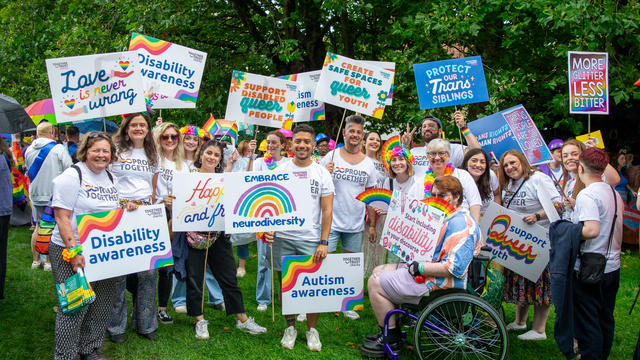 large group of people wearing rainbow clothing holding placards.