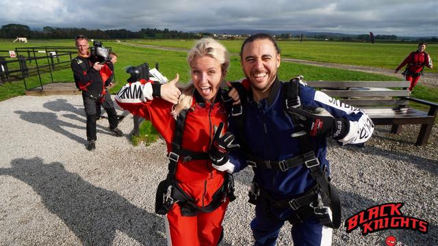 Two staff members smiling widely at the camera in their skydiving equipment