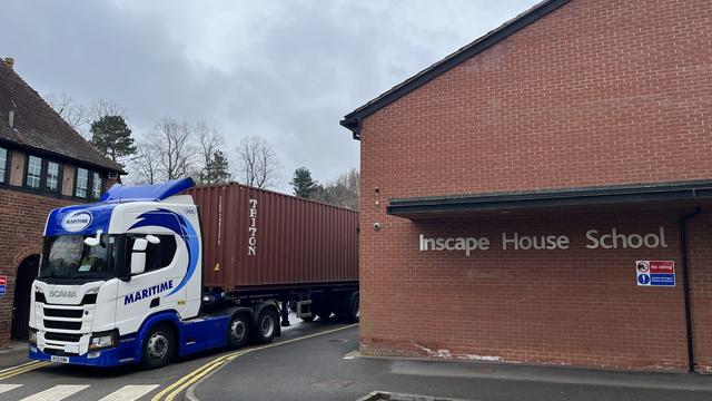 A lorry carrying the huge container next to the front entrance of Inscape House school.