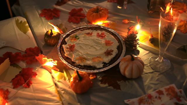 A pumpkin pie on a table decorated with autumn leaves and lights
