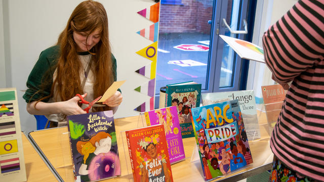 Teen girl sitting behind a table full of books on LGBTQ+ topics. 