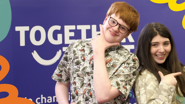 James and Jessica smile at camera behind blue Together Trust banner