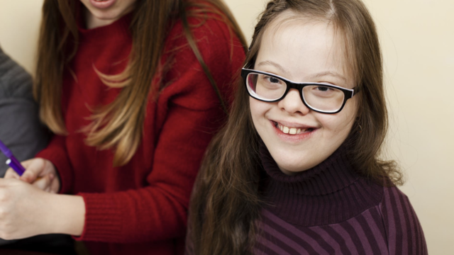 Child with down syndrome smiling. Sat next to woman whose face isn't visible.