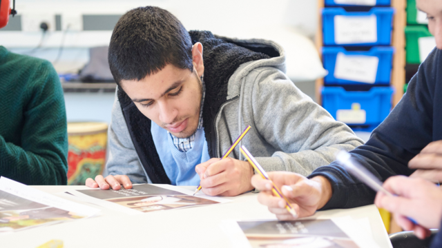 College student in a classroom focusing on a piece of coursework. He is writing down with a pencil next to other students doing the same. 