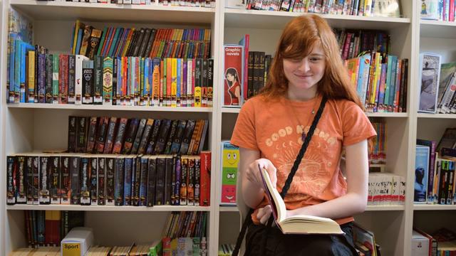 Talia sitting on a chair with a book in her hand in the school library at Inscape House School