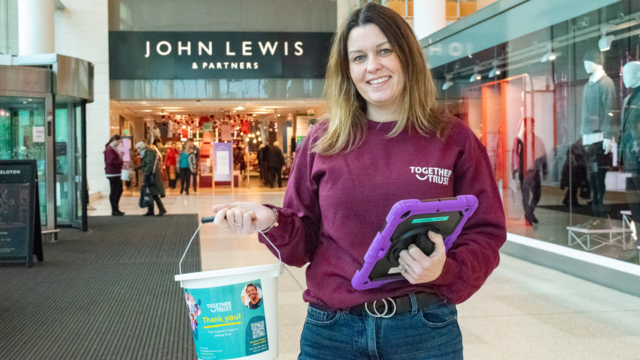 Woman holding up a donation bucket posing outside a shop