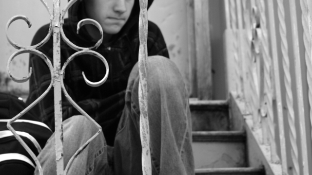 black and white photo of a teenager sitting down outside, on stairs, looking pensive 