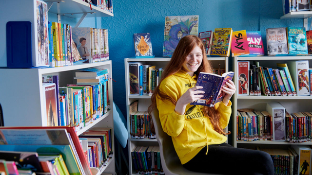 Young girl reading a manga comic book sitting down in a colorful school library