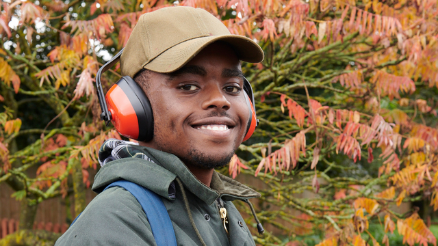 Man wearing noise cancelling headphones over a cap smiling. 