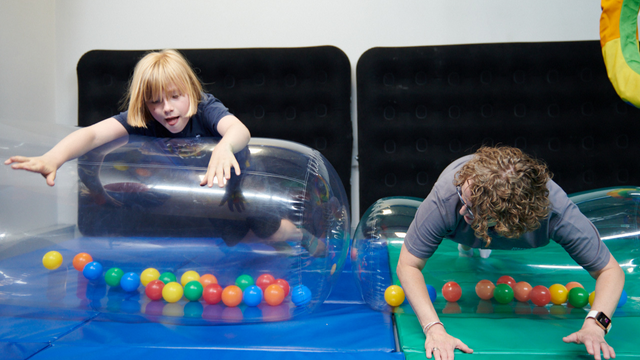 Young boy and adult woman rolling on inflatable tubes in a soft play area.
