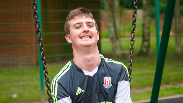 Teenage boy sitting down on a swing smiling at the camera