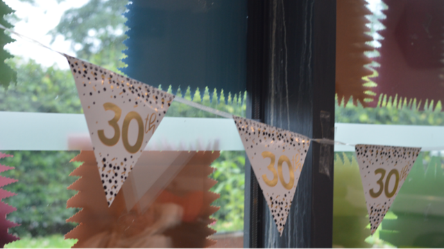 A photograph of bunting hung in front of a window. It's decorated with gold text "30th' 