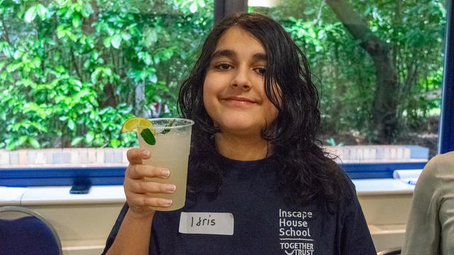 Young boy holding up a plastic cup. He is showing the alcohol-free mojito he made and smiling. 
