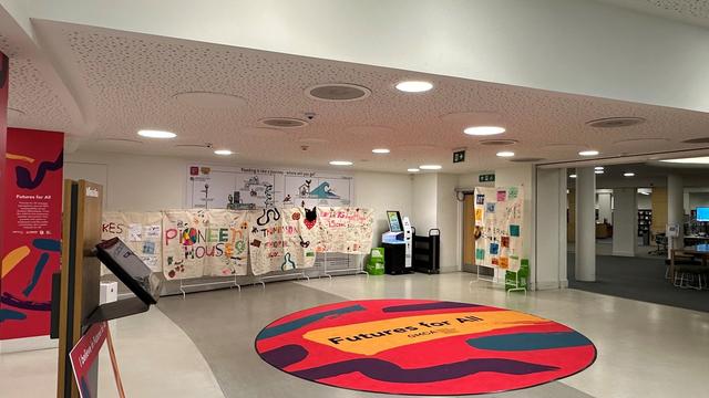 A wide panoramic photo of the gallery exhibition displaying multiple large textile panels of art. 