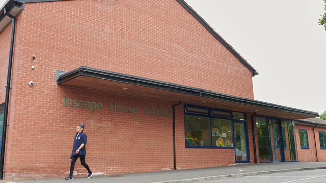 A staff member walks by a large brick building that says Inscape School across the side.