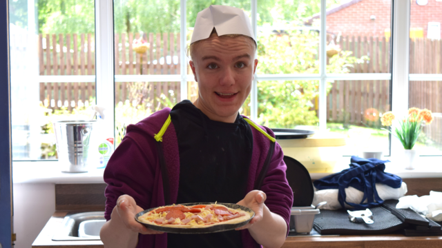 A student smiling while showing the pizza his pizza.