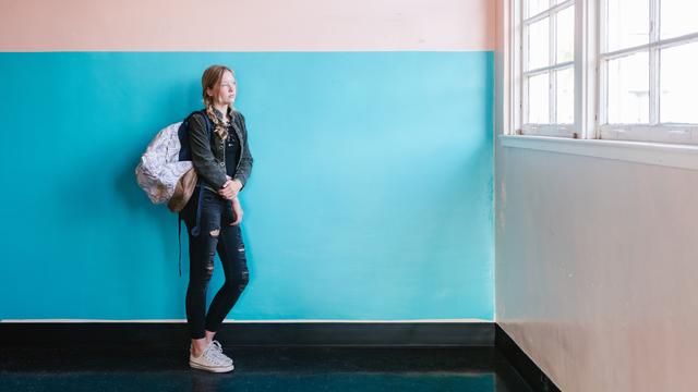 Young woman stands in front of a bright blue and white painted wall, looking out the window.