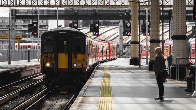 Person waiting behind the yellow line in on a train station platform. A train is approaching the platform. 