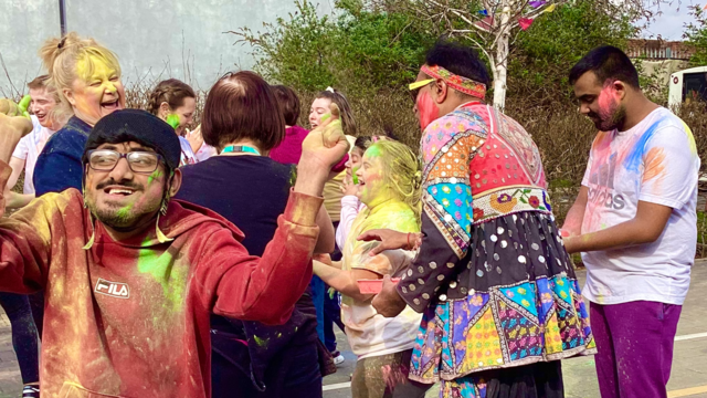 Students cheering, laughing and smiling as they throw coloured powdered paint in to the air. They are covered in bright colourful paint!  